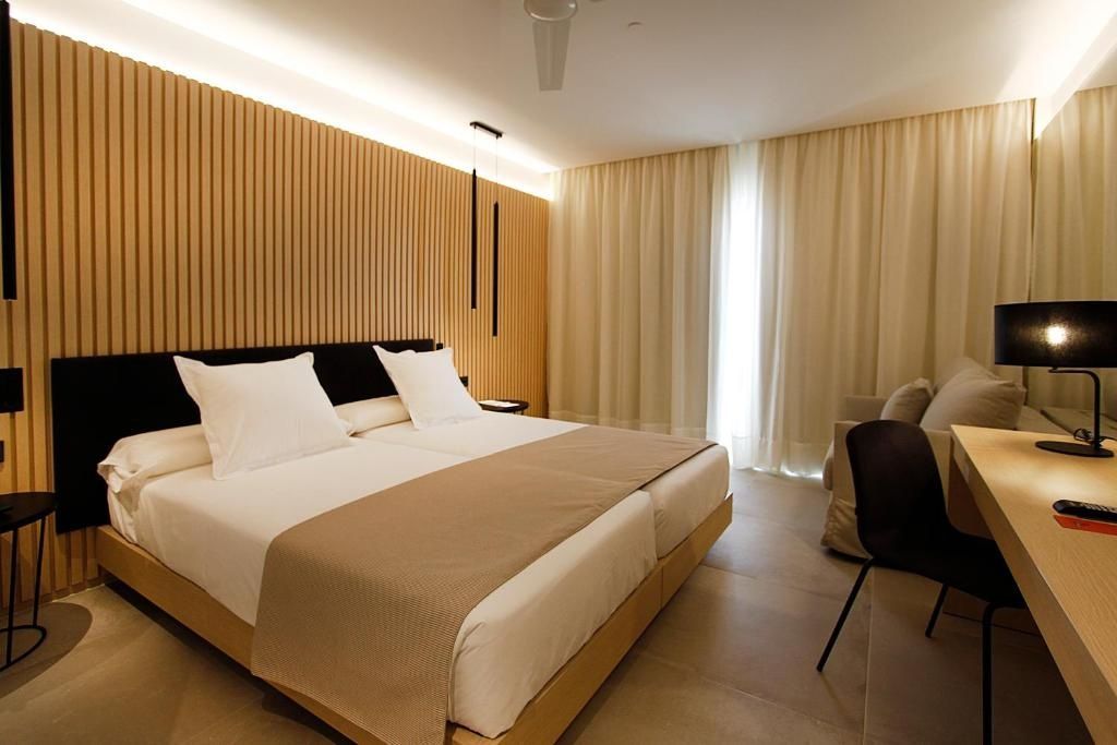 Doppelbett mit weißer Bettwäsche und brauner Tagesdecke vor einer Holzlamellenwand.