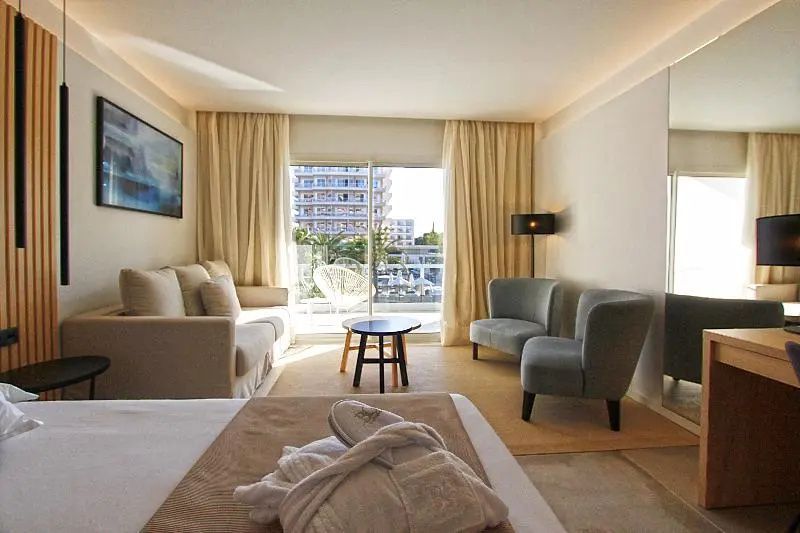 Wohnbereich im Hotelzimmer mit hellem Sofa, zwei grau grünen Sesseln und Balkonausgang