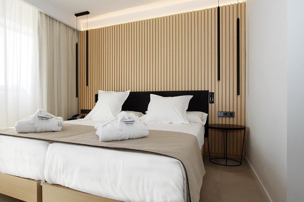 Doppelbett im Hotelzimmer mit Holzlamellenwand, Nachttisch und hängenden Lampen.