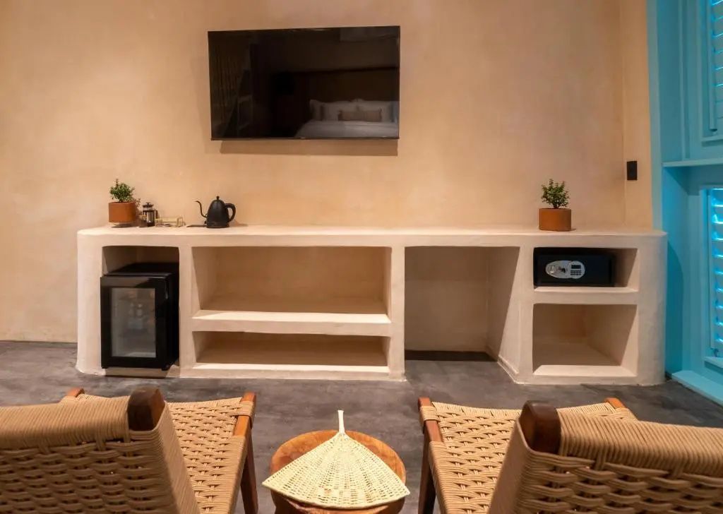 Sitzbereich im Hotelzimmer mit zwei Flechtsesseln, Fernseher und offenem Schrankregal.