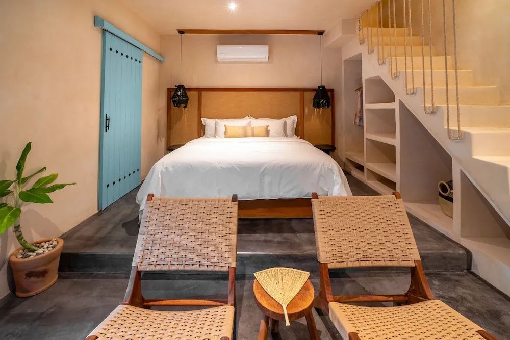Hotelzimmer mit großem Doppelbett, Holzstühlen und hellblauer Schiebetür.