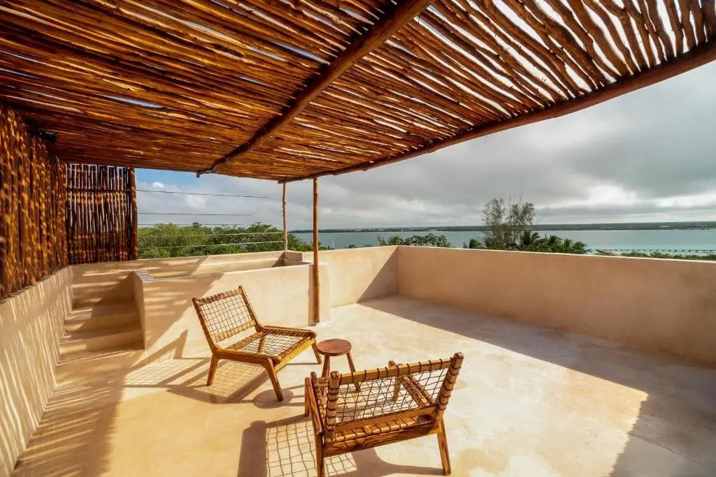 Sonnige Terrasse mit Holzpergola, zwei Holzstühlen und Ausblick auf das Wasser.