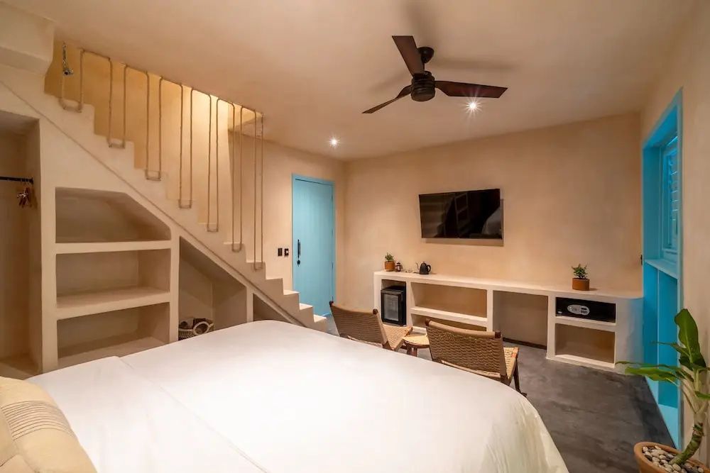 Zimmer mit Treppe, weich bezogenem Bett, Deckenventilator und hellblauer Tür.