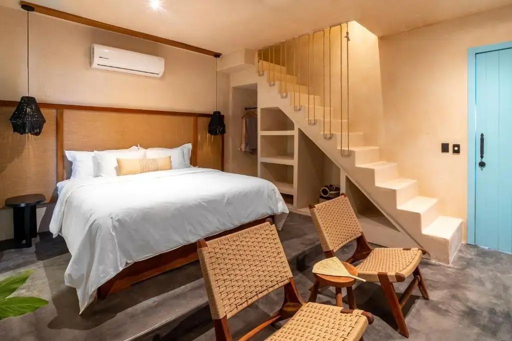 Helles Hotelzimmer mit Doppelbett, Treppe und zwei Stühlen im Vordergrund.