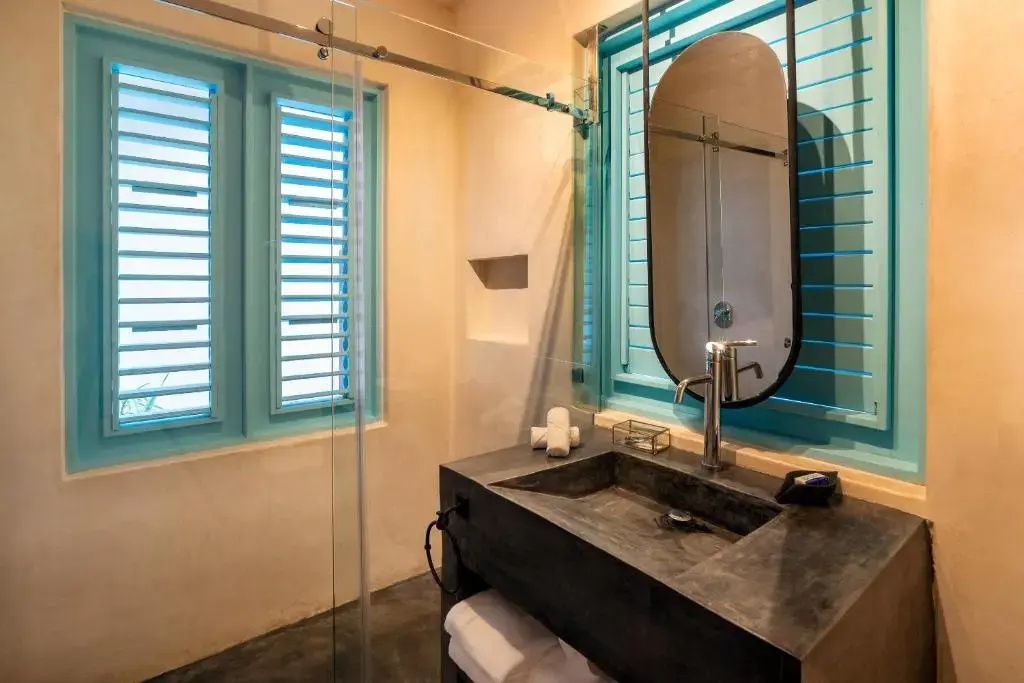 Badezimmer mit dunklem Waschtisch, ovalem Spiegel, Glasdusche und blauen Fenstern.
