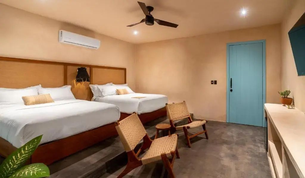 Schlafbereich mit zwei Doppelbetten, Holzstühlen und Deckenventilator im Zimmer.