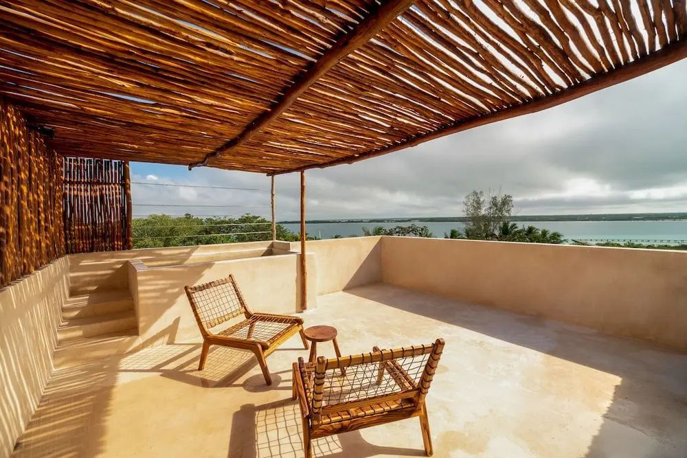 Sonnige Dachterrasse mit Holzstühlen, Pergola und Weitblick über das Wasser.