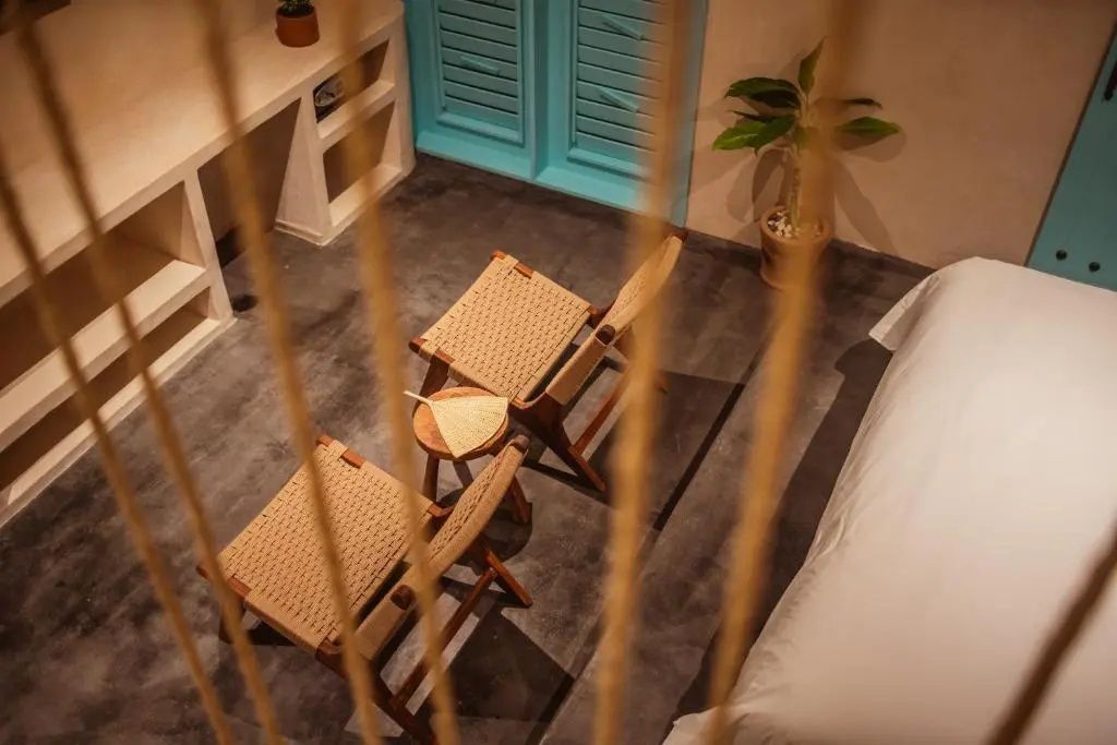 Sitzecke im Hotelzimmer mit zwei Flechtstühlen, Holzbeistelltisch und Pflanze.
