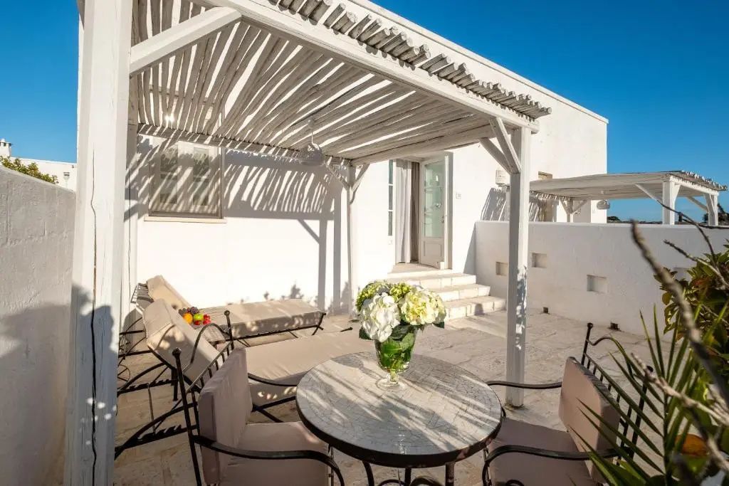 Sonnige Terrasse mit Holzpergola, Liegestühlen und einem Tisch mit Stühlen