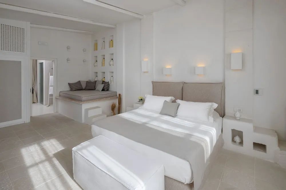 Hell gestaltetes Schlafzimmer mit Doppelbett, Wandleuchten und separater Sitzecke.