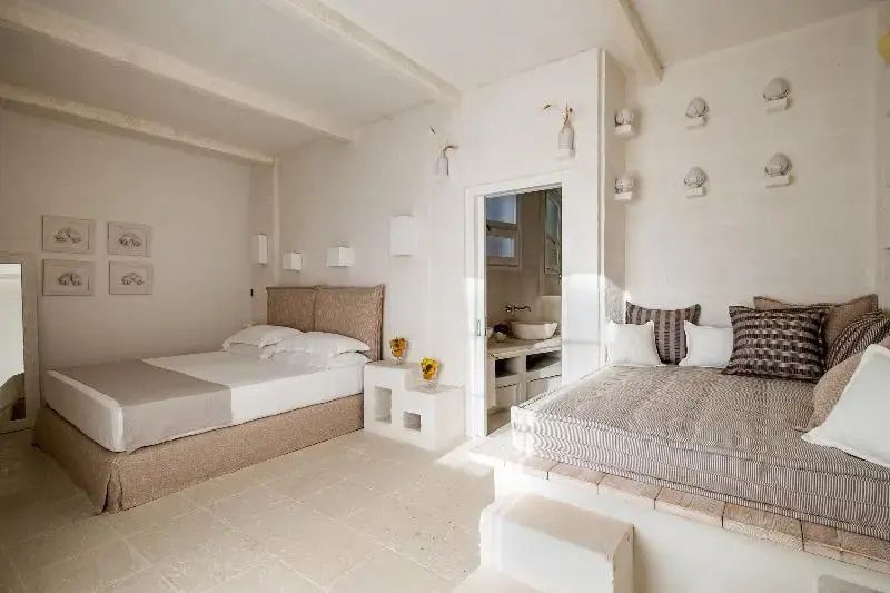 Helles Hotelzimmer mit Doppelbett, Sitzbereich auf Podest und Durchgang zum Badezimmer.