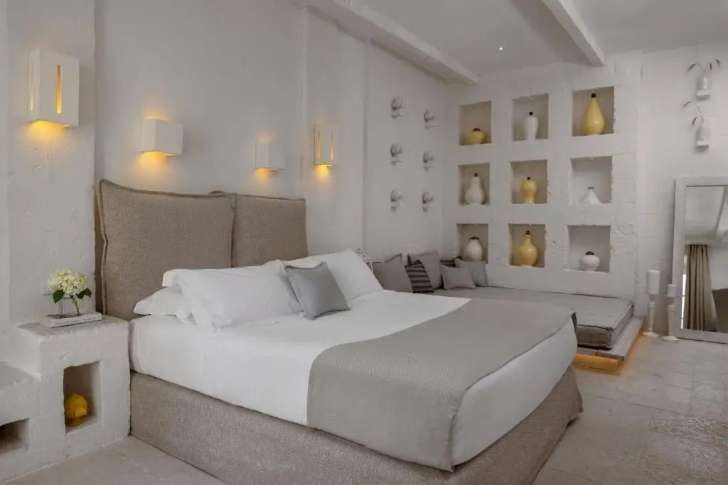 Schlafzimmer mit großem Doppelbett, Wandbeleuchtung und Nischen mit dekorativen Vasen.