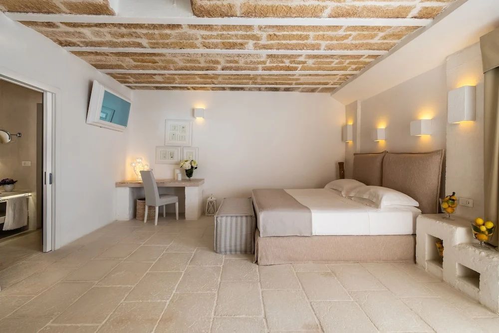 Schlafzimmer mit Doppelbett, hellem Steinboden, Gewölbedecke und einem kleinen Schreibtisch.
