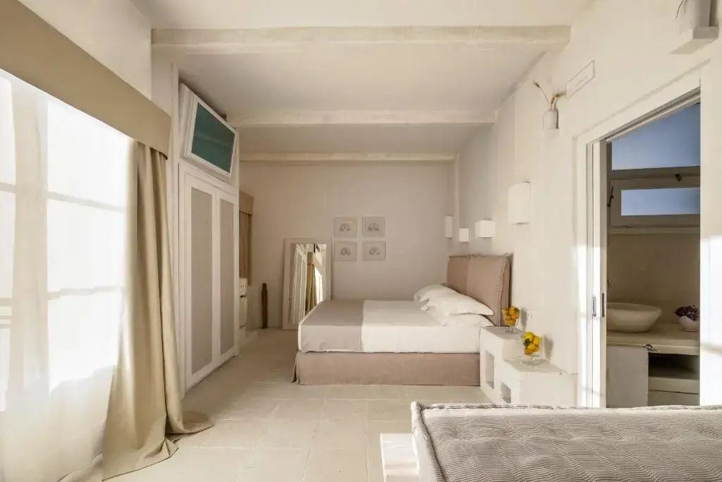 Hell eingerichtetes Schlafzimmer mit beige verkleidetem Doppelbett und hellem Fliesenboden.