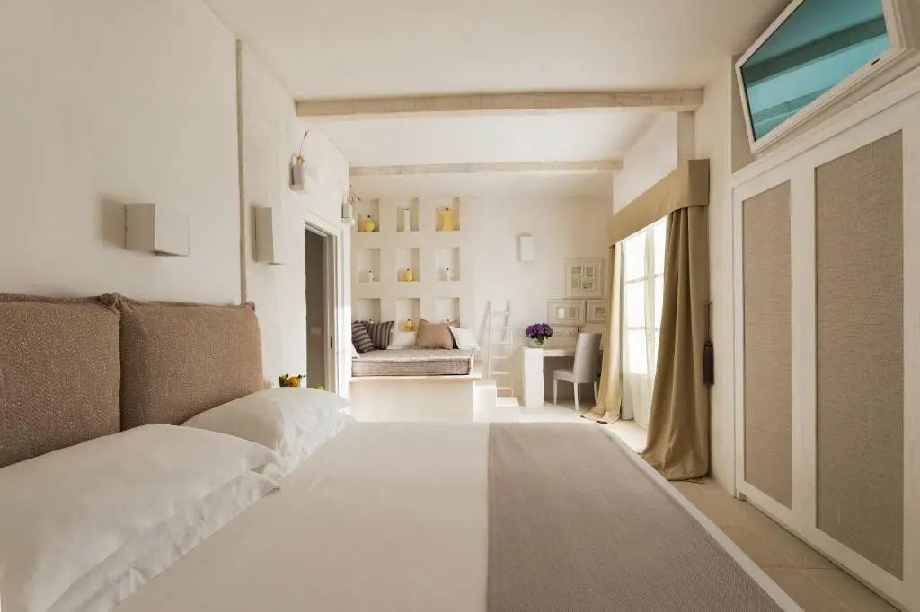 Blick in ein helles Zimmer mit Doppelbett im Vordergrund und einem Arbeitsplatz im Hintergrund.