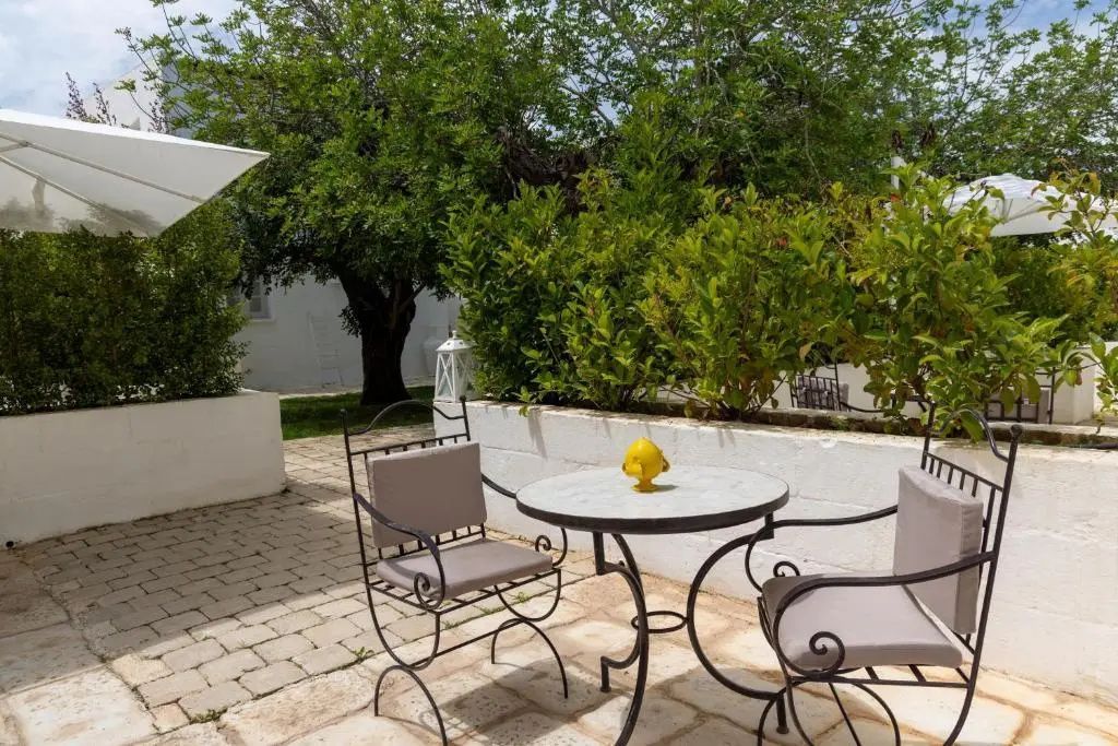 Sitzbereich im Freien mit schmiedeeisernen Stühlen und einem runden Tisch auf gepflasterter Terrasse.