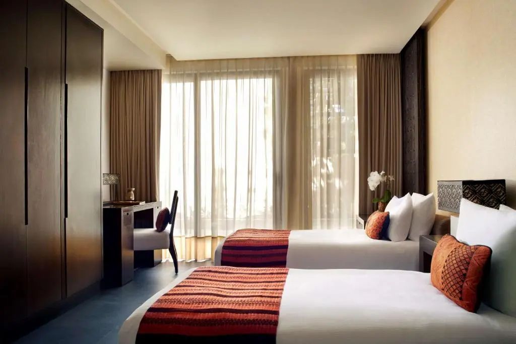 Schlafzimmer mit zwei Einzelbetten, orangefarbenen Läufern und hellem Fensterbereich.