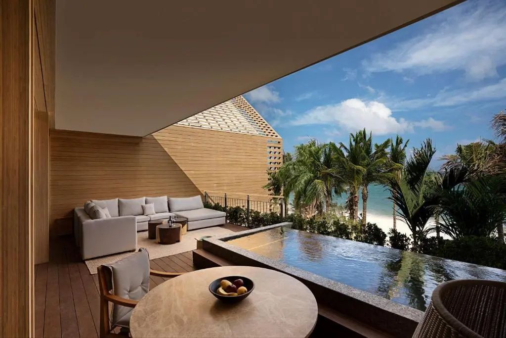 Überdachte Terrasse mit Loungebereich, kleinem Pool und Blick auf Palmen und Meer.