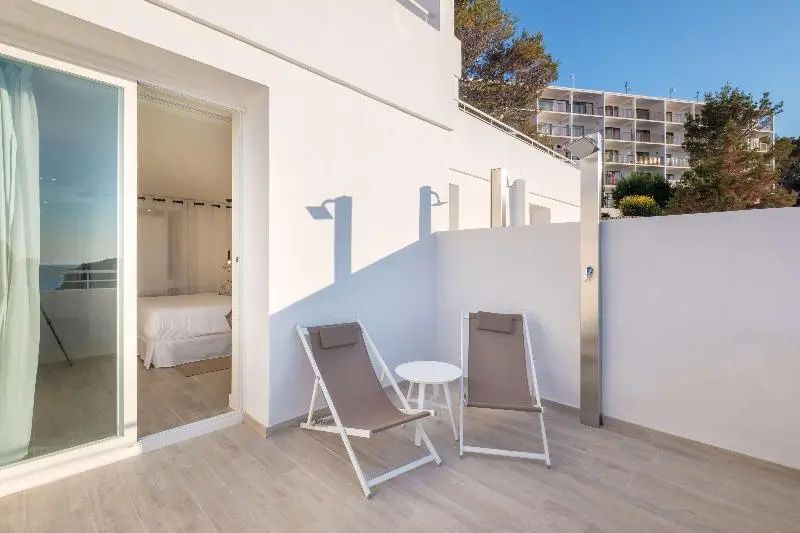 Terrasse mit zwei Klappstühlen, kleinem Tisch und einer Außendusche vor weißer Wand.