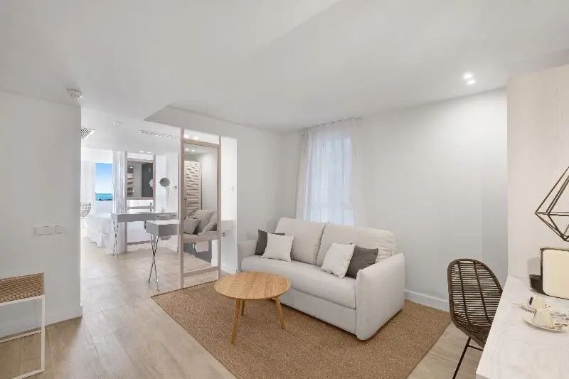 Wohnbereich eines Hotelzimmers mit hellem Sofa, Holzcouchtisch und beigem Teppich.