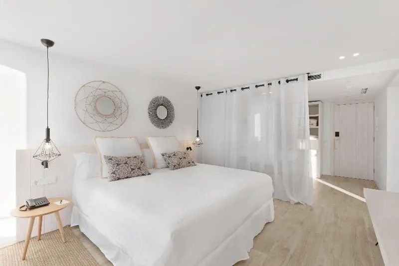 Helles Schlafzimmer mit weißem Bett, Wanddekoration und transparentem Raumteiler.