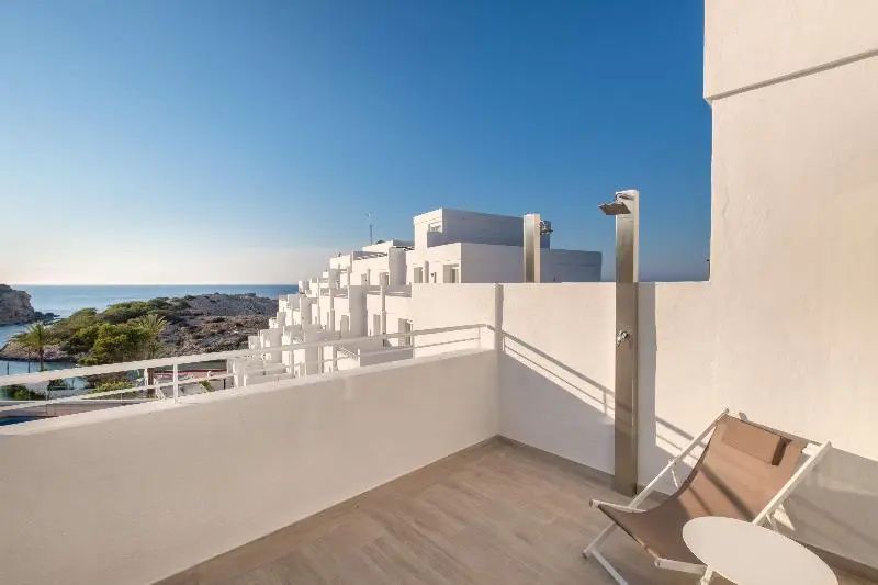 Balkon mit Außendusche und Ausblick auf weiße Hotelgebäude und das Meer.