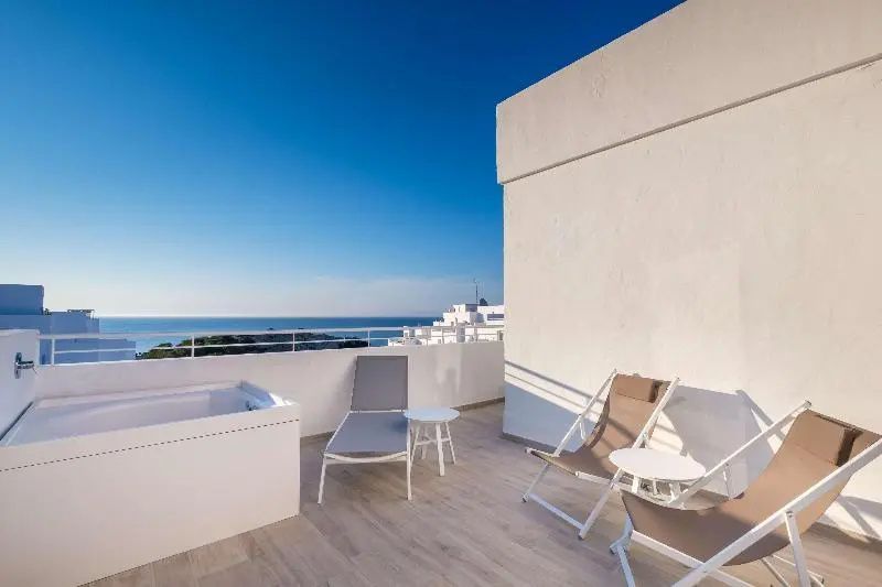 Sonnenterrasse mit Whirlpool, Sonnenliege, Stühlen und Blick auf das Meer.