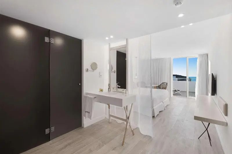 Offener Waschtischbereich mit weißem Waschbecken und Blick in das helle Hotelzimmer