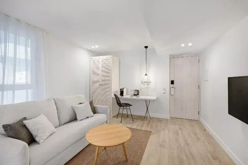 Sitzbereich im Hotelzimmer mit Sofa, Holztisch, Schreibtisch und hellem Schrank.
