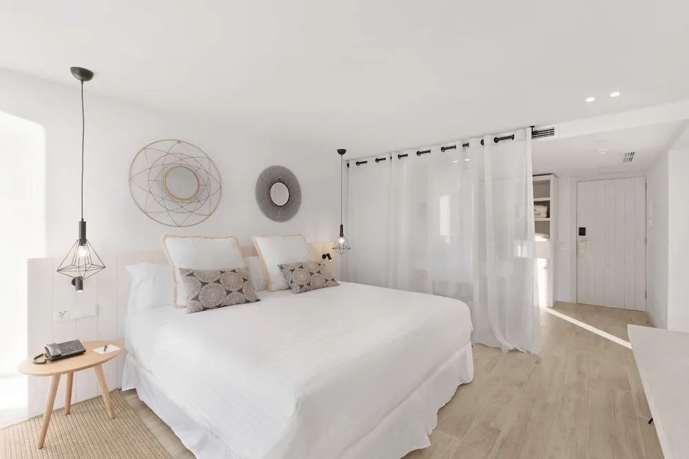 Helles Doppelzimmer mit weißer Bettwäsche, runden Wandspiegeln und einem transparenten Vorhang.