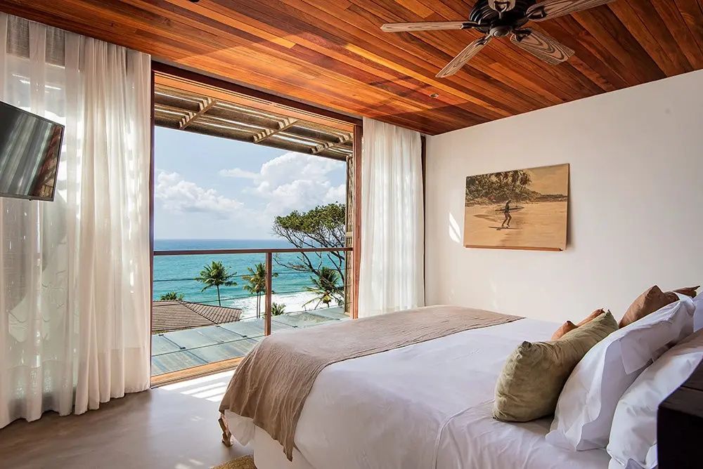Schlafzimmer mit Holzdecke und weiter Öffnung zum Balkon mit Meerblick.