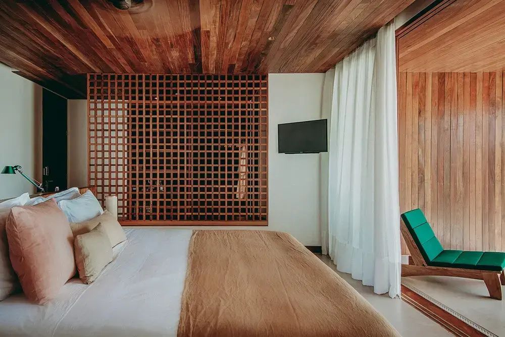 Schlafzimmer mit Holzdecke, Gitterwand aus Holz, großem Bett und Blick zur Terrasse.