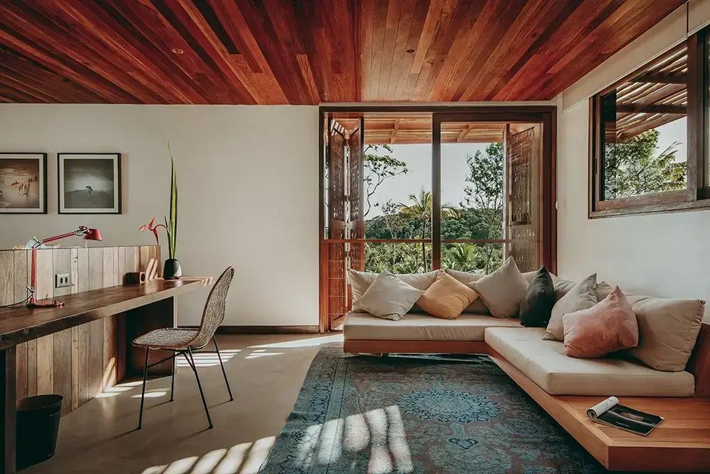 Wohnbereich mit großem Sofa, gemustertem Teppich und Blick auf tropische Pflanzen.