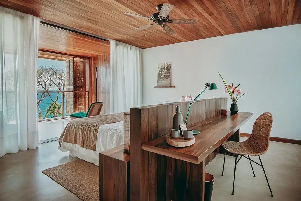 Einrichtungsbeispiel eines Zimmers mit Holzschreibtisch, Deckenventilator und Meerblick.