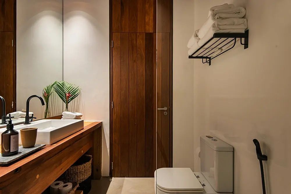 Badezimmer mit hölzernem Waschtisch, Spiegel, Toilette und Handtuchablage.
