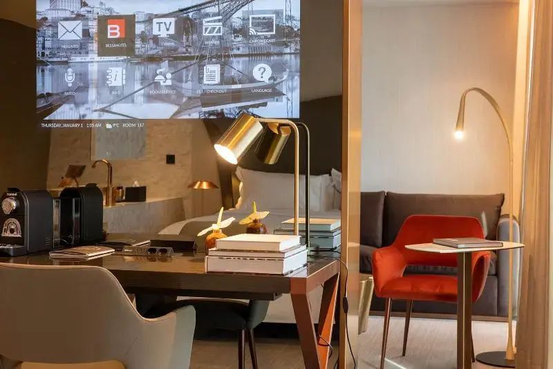 Schreibtisch mit goldener Lampe, rotem Stuhl und Projektion an der Wand.