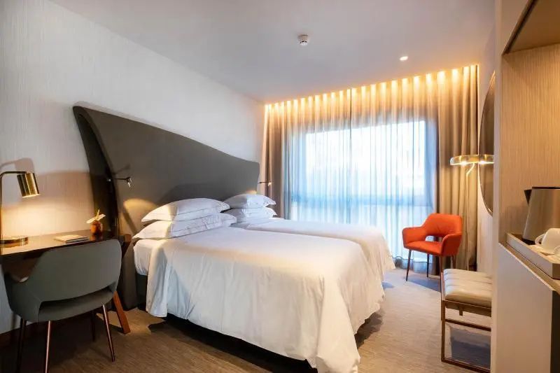 Modernes Hotelzimmer mit zwei Einzelbetten, warmem Licht und rotem Sessel.