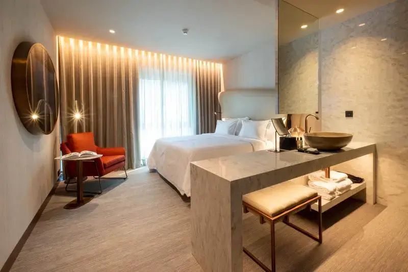 Hotelzimmer mit Doppelbett, rotem Sessel und offen integriertem Waschtisch.