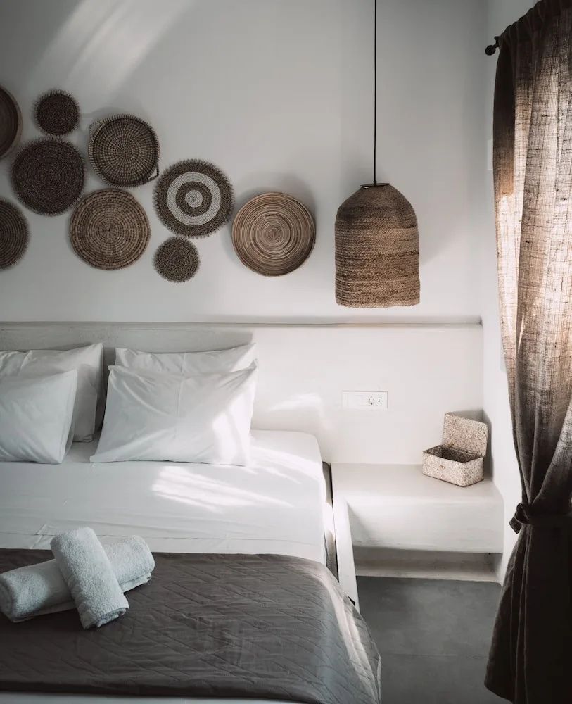 Weißes Doppelbett mit grauer Tagesdecke und runden Flechtdekorationen an der Wand.