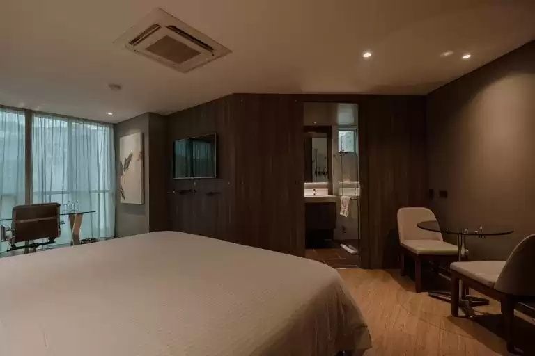 Modernes Hotelzimmer mit Holzoptik, Doppelbett, Wand-TV und Blick ins Badezimmer.