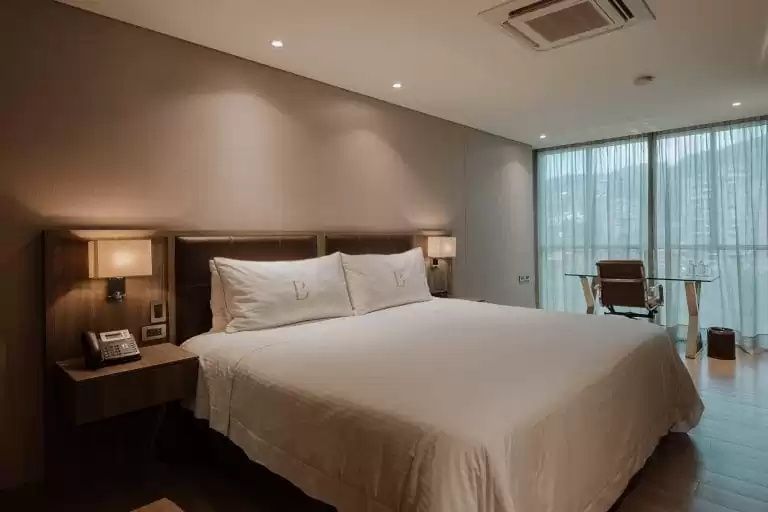 Geräumiges Hotelzimmer mit großem Doppelbett, Nachttischen und hellem Fensterbereich.