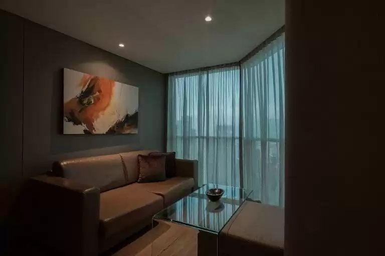 Sitzbereich im Hotelzimmer mit braunem Sofa, Glascouchtisch und bodentiefen Fenstern.