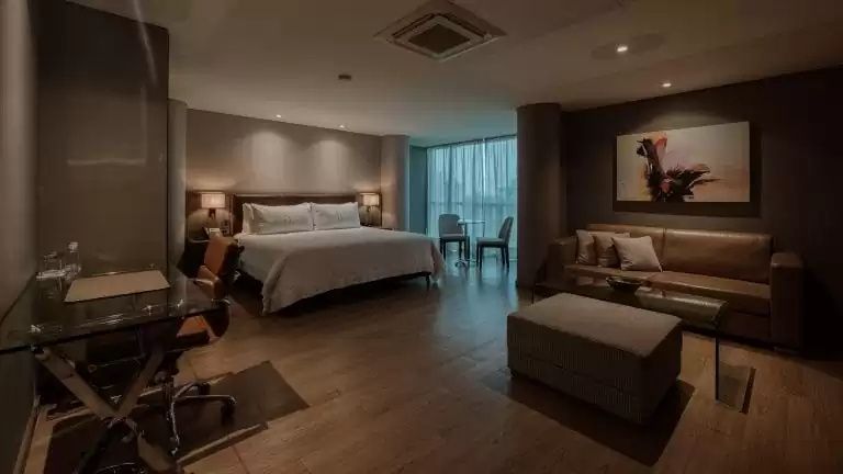 Großes Hotelzimmer mit Doppelbett, Sitzbereich mit Sofa und bodentiefen Fenstern.