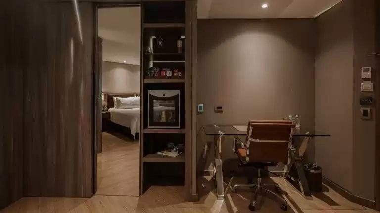 Schreibtisch mit Bürostuhl, Glasplatte, Regalelement und Blick ins Schlafzimmer.