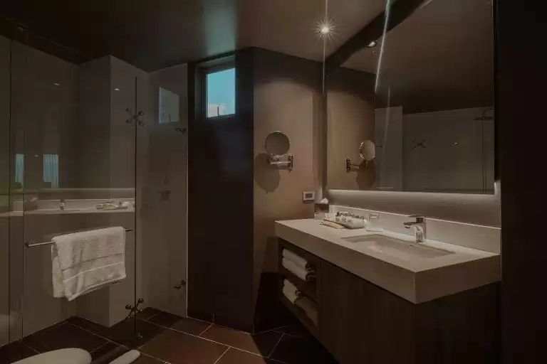 Badezimmer mit beleuchtetem Spiegel, großem Waschtisch und gläserner Duschtür.