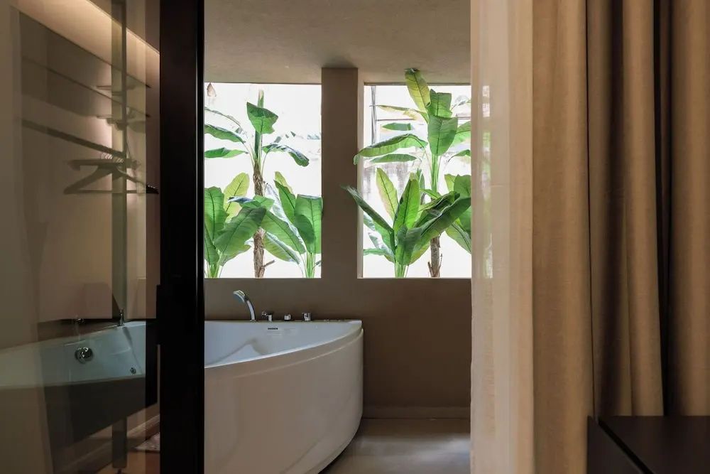 Weiße Eckbadewanne mit Blick auf grüne Pflanzen vor dem Fenster.