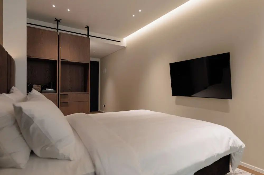Doppelbett mit weißer Bettwäsche, Fernseher an der Wand und offenem Kleiderschrank.