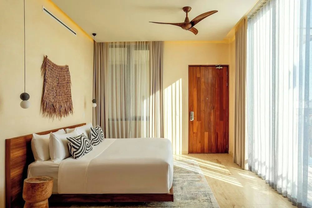 Schlafzimmer mit großem Doppelbett, Holz Eingangstür, Deckenventilator und Wanddeko.