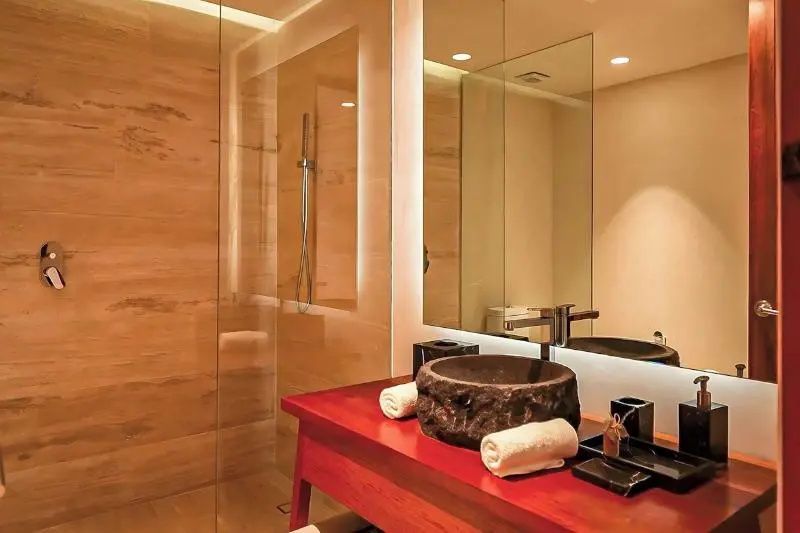 Badezimmer mit Steinwaschbecken auf rotem Holzwaschtisch und ebenerdiger Glasdusche.