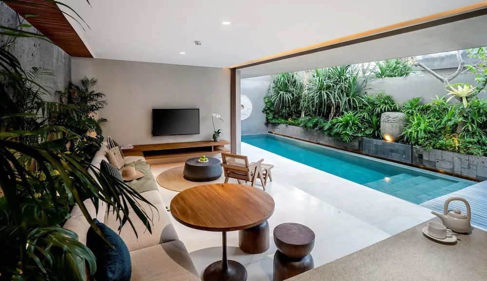 Offener Wohnbereich einer Villa mit Blick auf den privaten Pool und grüne Pflanzen.